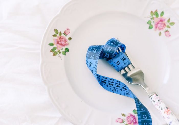 A floral plate with a blue measuring tape wrapped around a fork, symbolizing dieting.